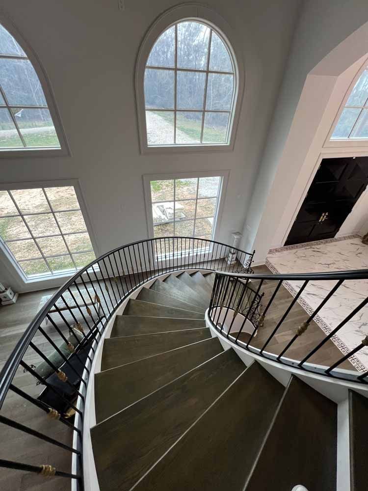 Spiral staircase with black railings beside tall arched windows in a bright interior
