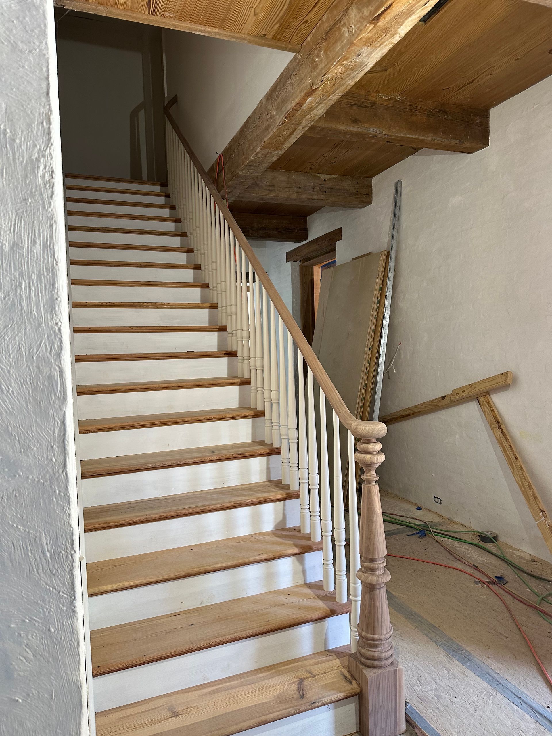 Indoor wooden staircase with white risers and a carved banister in an unfinished room
