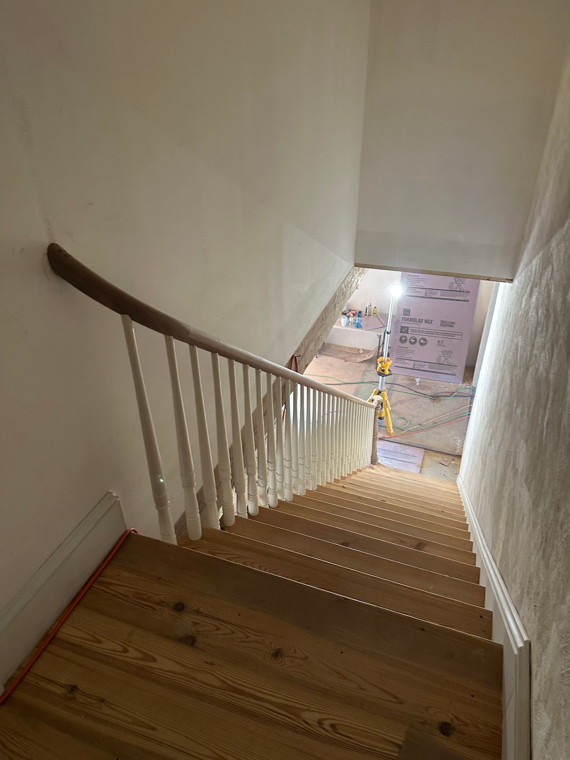 Staircase with wooden steps and white railing descending to a bright lower floor.