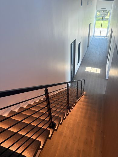 Staircase with black railing in a bright modern hallway, leading down to a sunlit window.