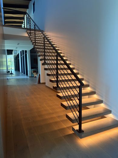 Modern indoor staircase with black railings and warm under-stair lighting in a minimalist home interior