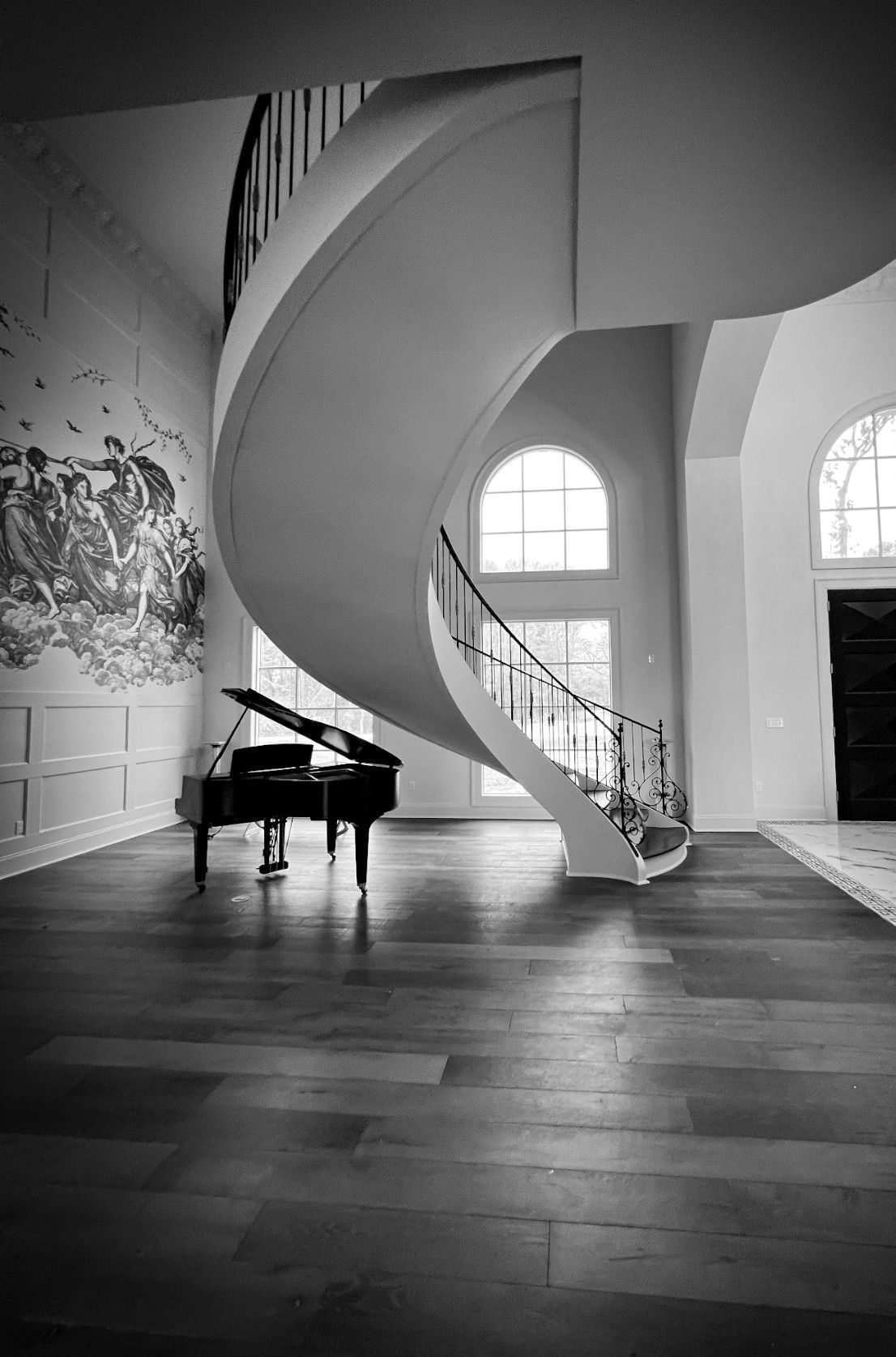 Black-and-white photo of a grand spiral staircase beside a grand piano in a bright hall