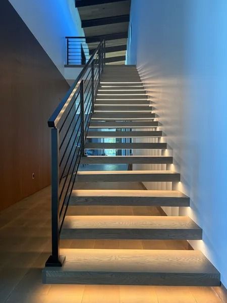 Modern indoor staircase with white walls, wood treads, black railing, and blue lighting.
