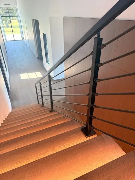 Interior staircase with wooden steps, black railing, and bright hallway light from a window.