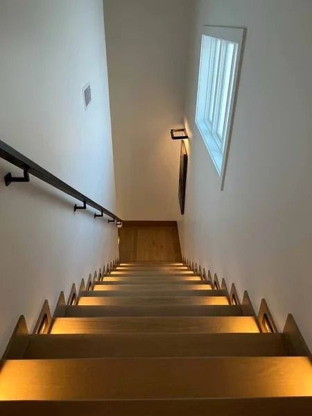 Narrow indoor staircase with wooden steps, white walls, and a window on the right.