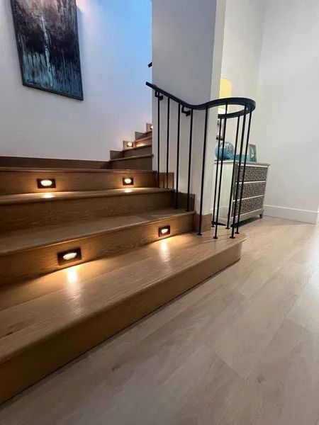 Modern indoor staircase with wooden steps, recessed lights, black railing, and light wood flooring