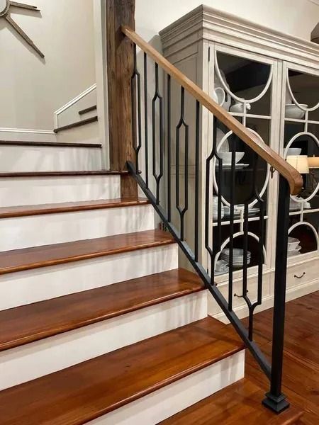 Staircase with polished wood steps, white risers, and black wrought-iron railing beside a cabinet.