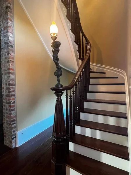Curved staircase with dark wood railing and a lit lamp post in a home interior
