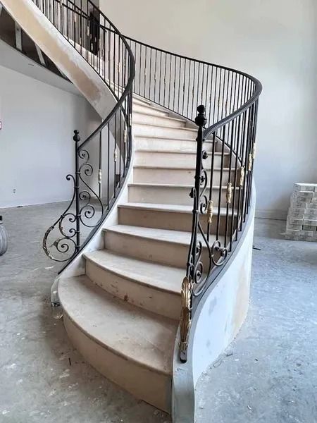Curved indoor staircase with white steps and ornate black iron railing in an unfinished room