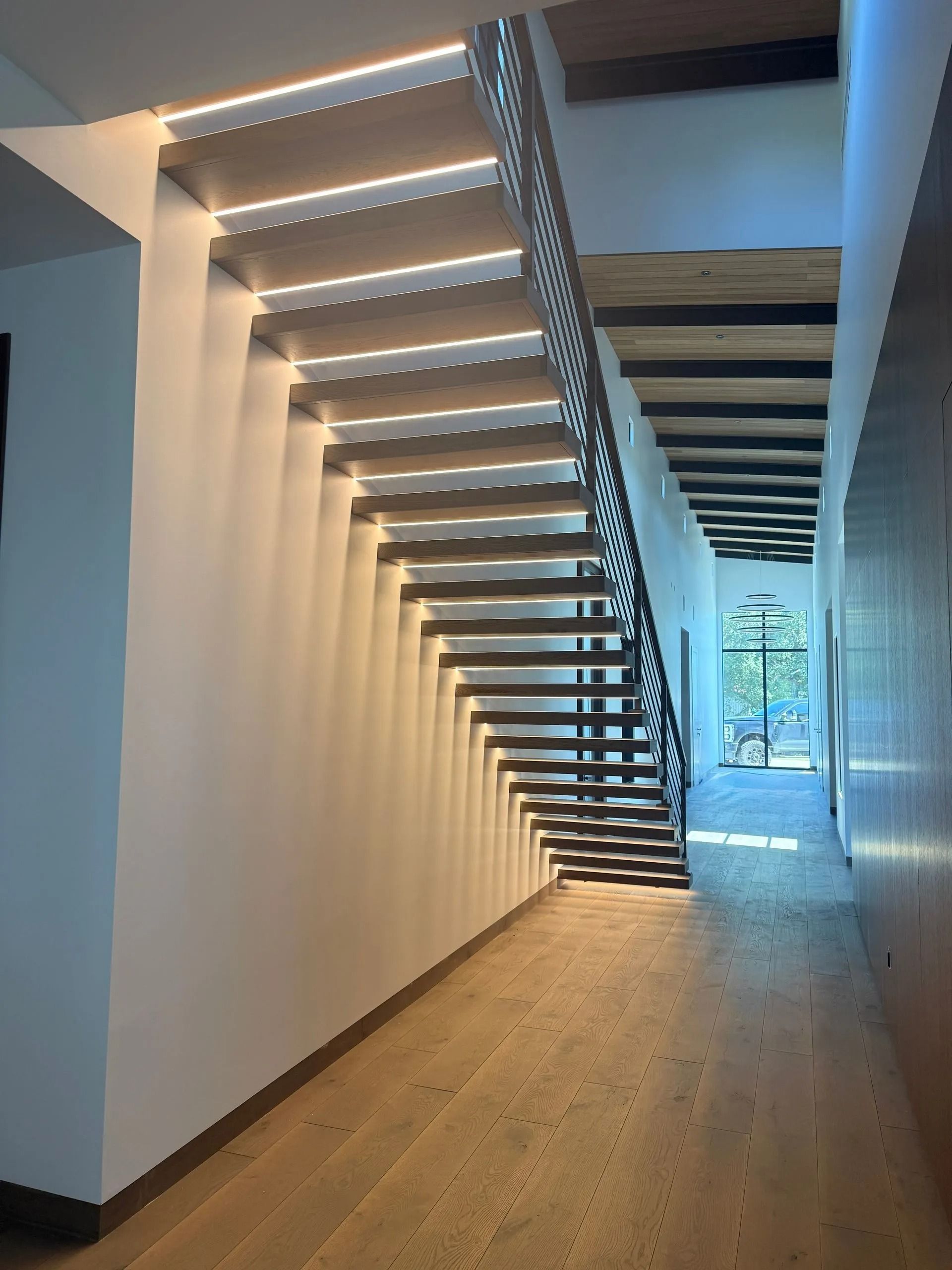 Modern hallway with floating staircase, wood floor, and skylight-lit corridor