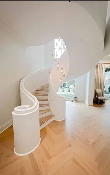 Curved white staircase in a bright modern home with light wood floors and a chandelier opening.