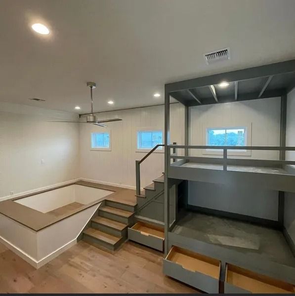 Empty modern loft interior with stairs, loft bed, white walls, wood floor, and large windows