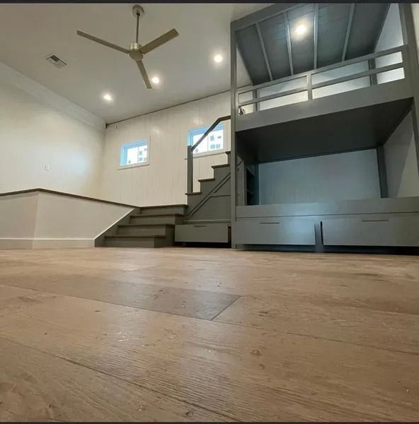 Empty modern room with wood floor, white walls, ceiling fan, stairs, and a lofted bunk area