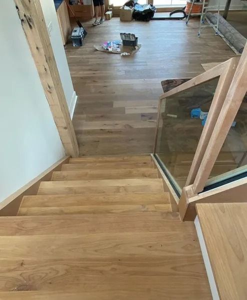 Wooden staircase descending into a cluttered room with hardwood floors and scattered items.