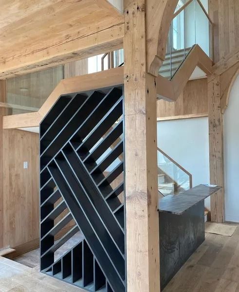 Wooden interior with a black slatted staircase or sculptural structure beneath exposed beams