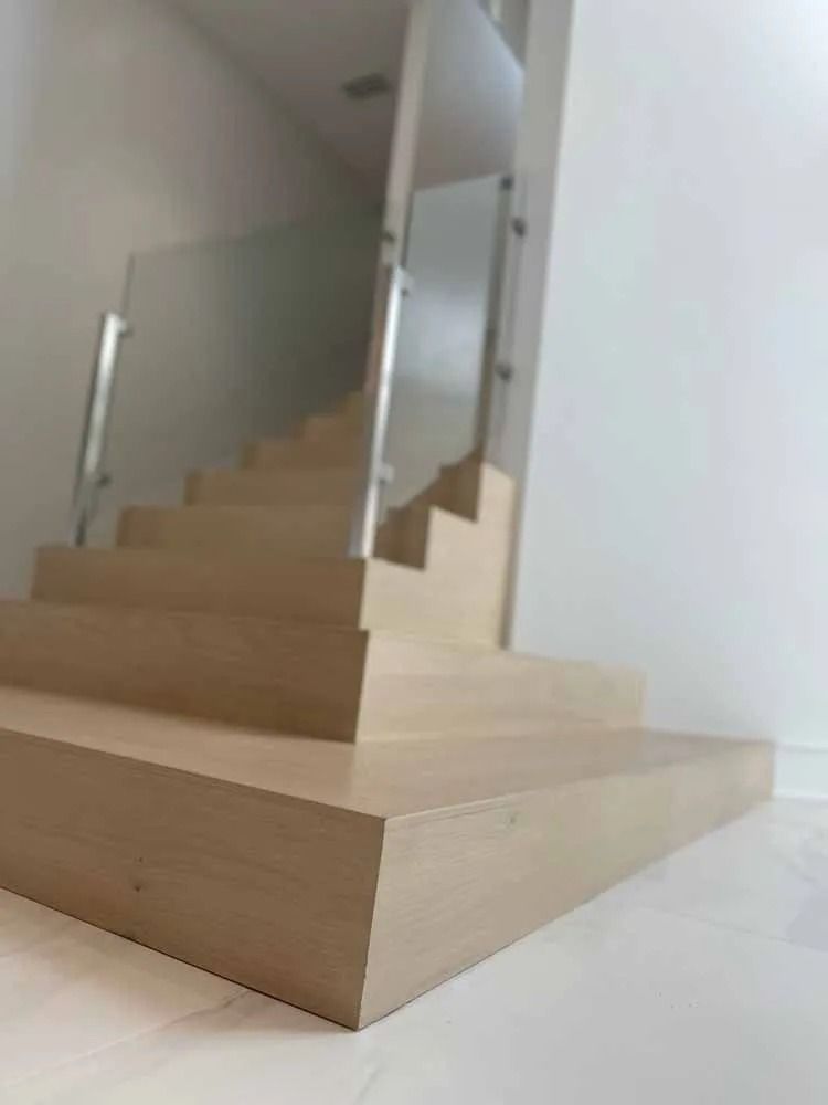 Light wood staircase with a glass railing in a minimalist white interior.