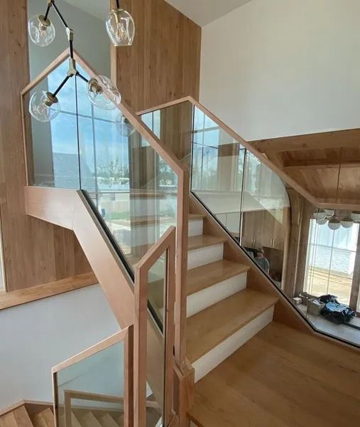 Modern indoor staircase with wood steps, glass railings, and skylight in a bright home interior