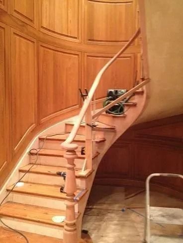 Wooden staircase with a white curved handrail and a stairlift chair on the steps, inside a wood-paneled home