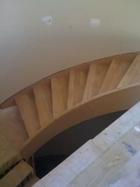 Wooden spiral staircase viewed from above, with beige walls and a dark center opening