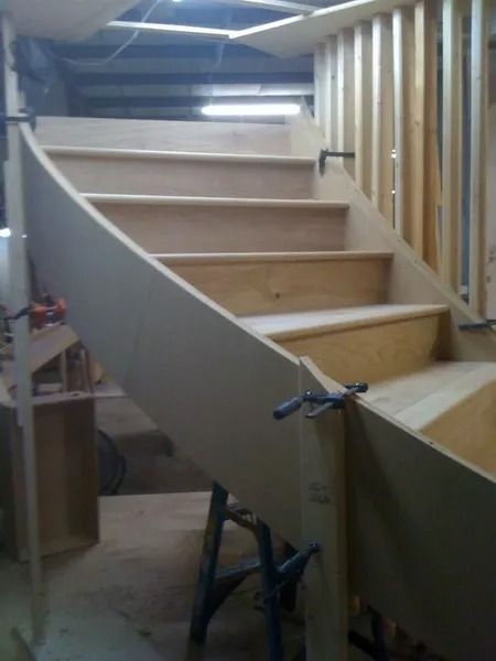 Partially built wooden staircase with curved side panel in a workshop, clamped in place