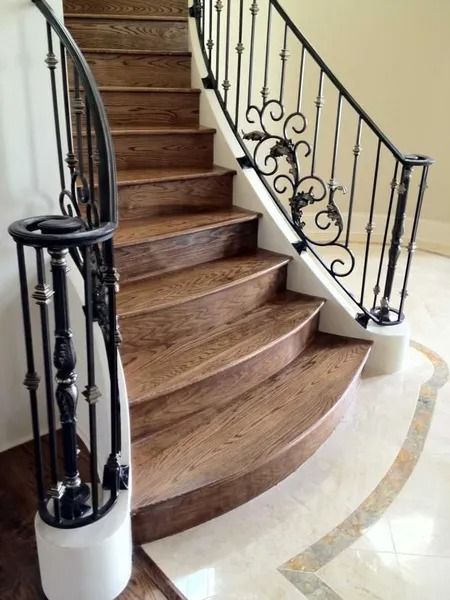 Curved wooden staircase with black wrought-iron railing and marble floor