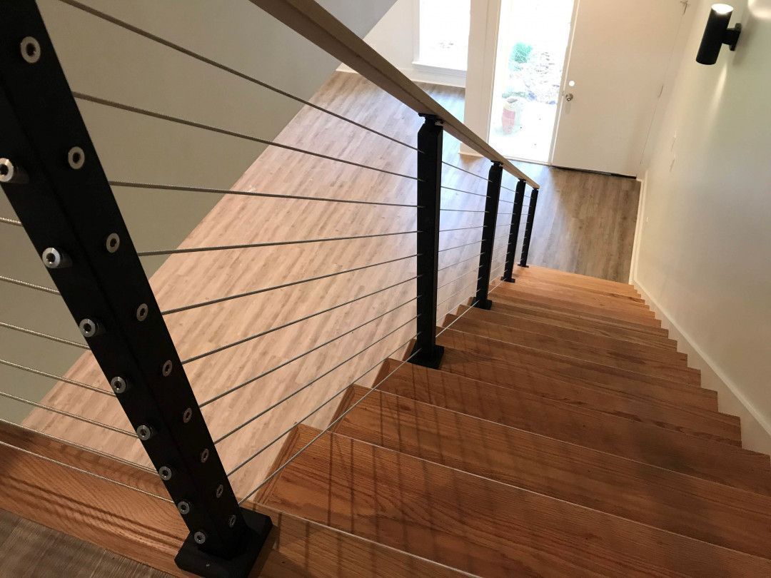 Staircase with wooden steps, black cable railing, and white walls in a narrow hallway.