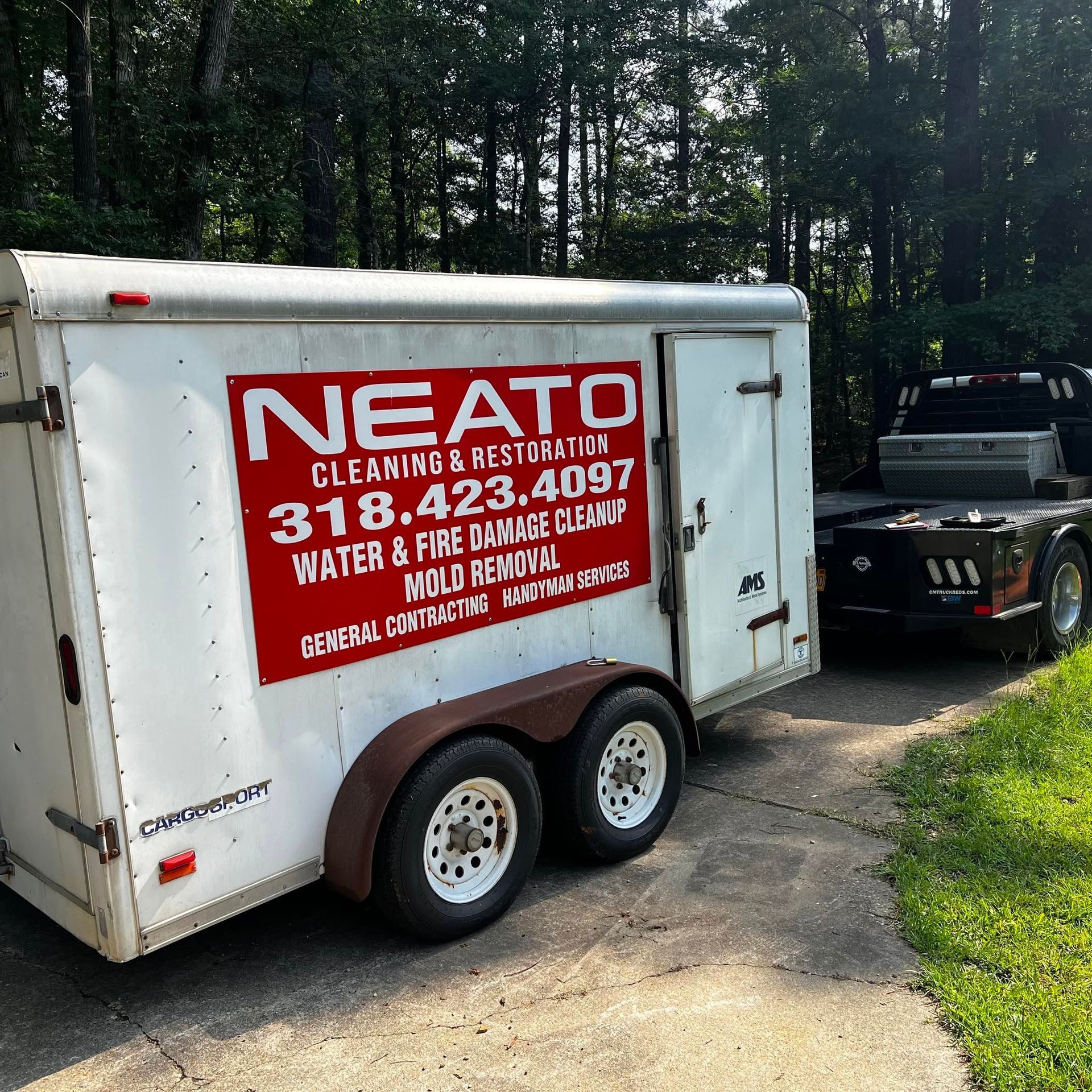 White cleaning trailer with red “Nesato Cleaning & Restoration” logo parked on a wooded driveway.