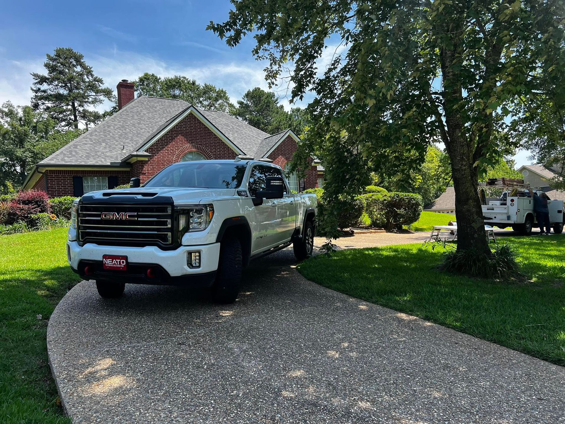 White pickup truck parked on a curved driveway beside a brick house with trees and a lawn