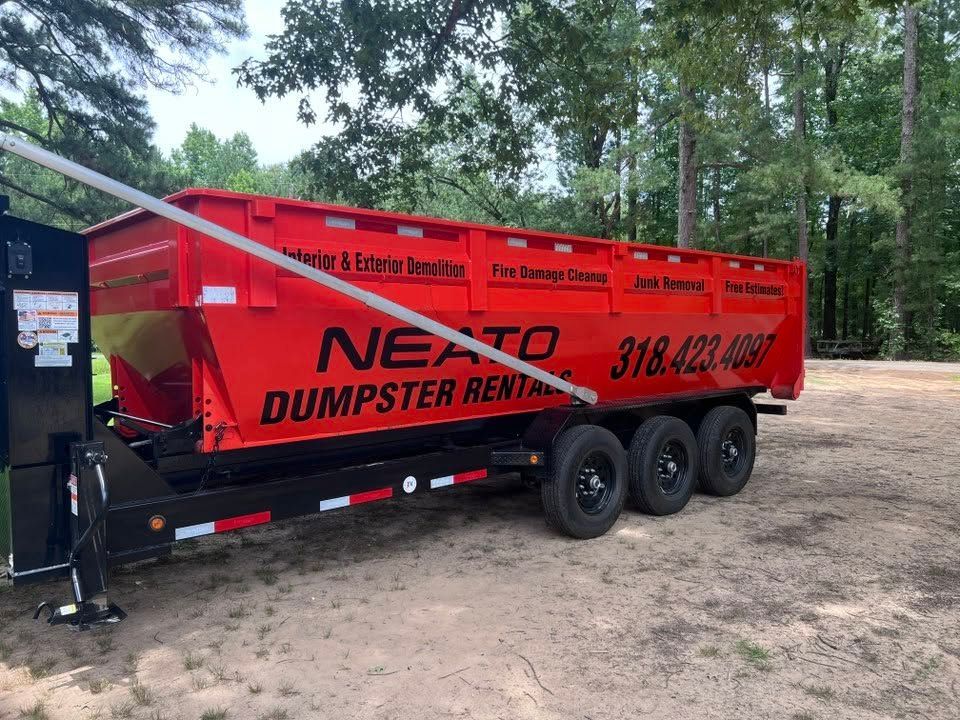 Red Nexpro dumpster rental trailer parked on a gravel lot beside trees and a utility shed.