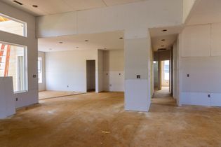 Empty unfinished interior with white walls, exposed drywall, and a bare wooden floor.