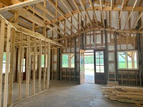 Unfinished wooden house interior with exposed framing, open doorway, and stacked lumber on the floor.