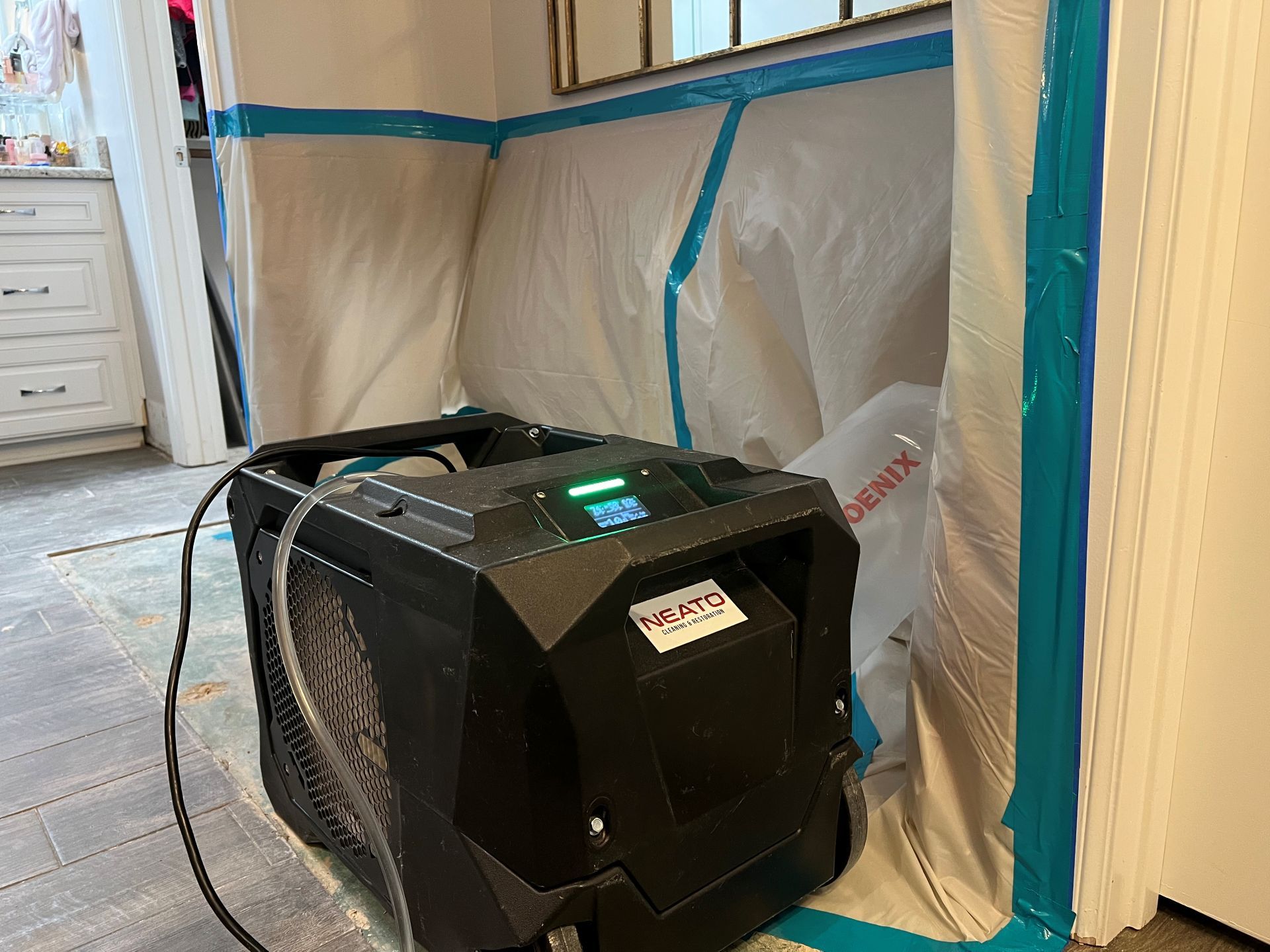 Black portable air scrubber with hose in a taped-off room under renovation.