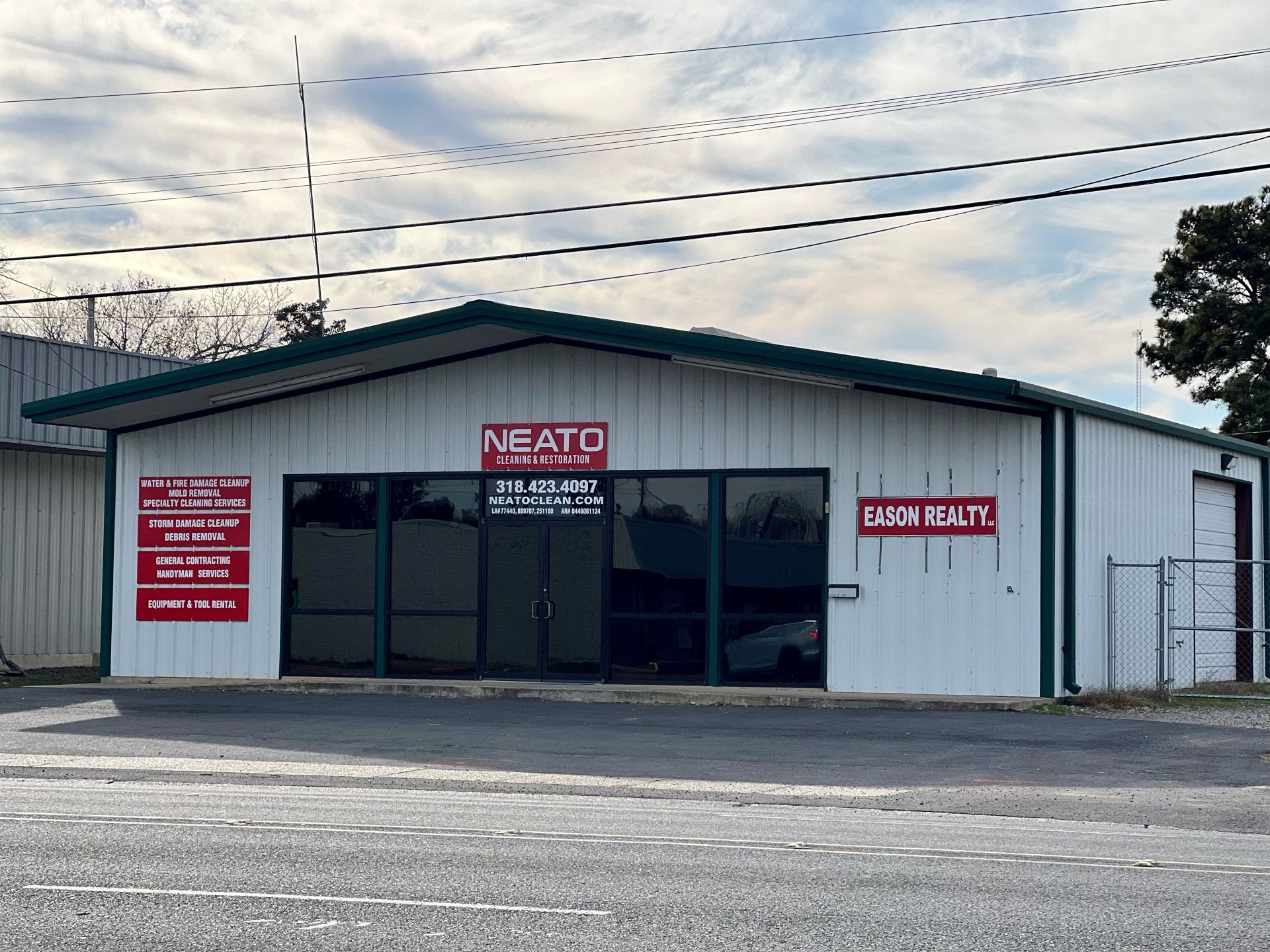 Small white industrial building with a red “NEATO” sign and parking lot in front