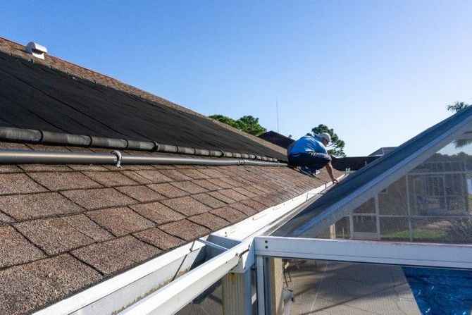 Rooftop workers repairing shingles beside a white metal roof edge under a clear blue sky