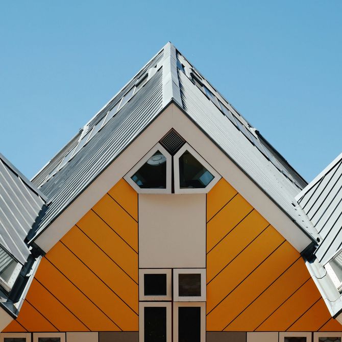Modern house facade with bright orange panels and a steep gray roof against a blue sky
