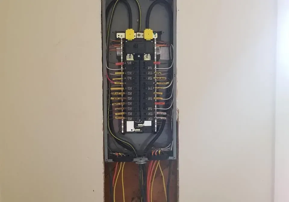 Electrical panel inside a wall cavity, showing circuit breakers, wiring, and conduits.