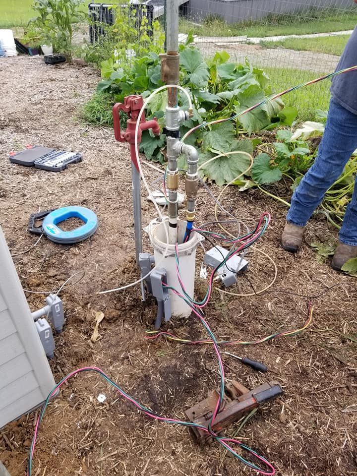 Well equipment with wires and tubing in a garden setting; person in jeans.