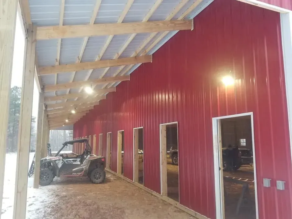 Red metal barn with open stalls and wooden porch; an ATV is parked beneath the porch.