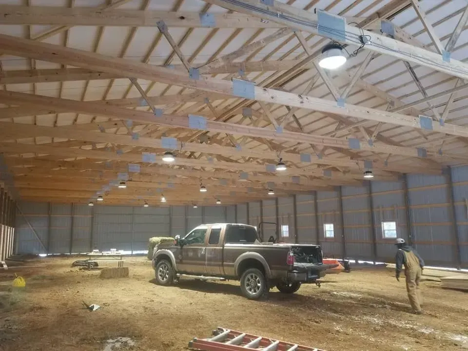 Inside a barn with a brown pickup truck, bales of hay, and a person walking.