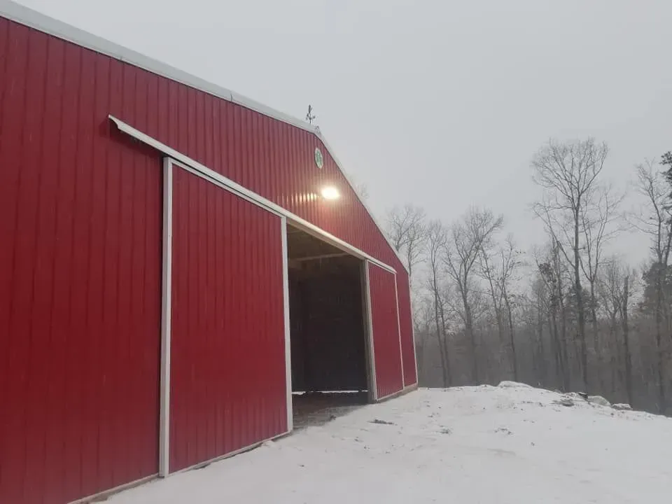 Red barn with open sliding doors and a lit entrance on a snowy day.