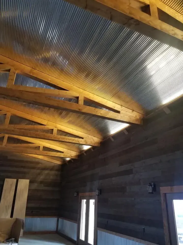 Interior view of a rustic building with a corrugated metal ceiling and wood beams. Wood-paneled walls and natural light.