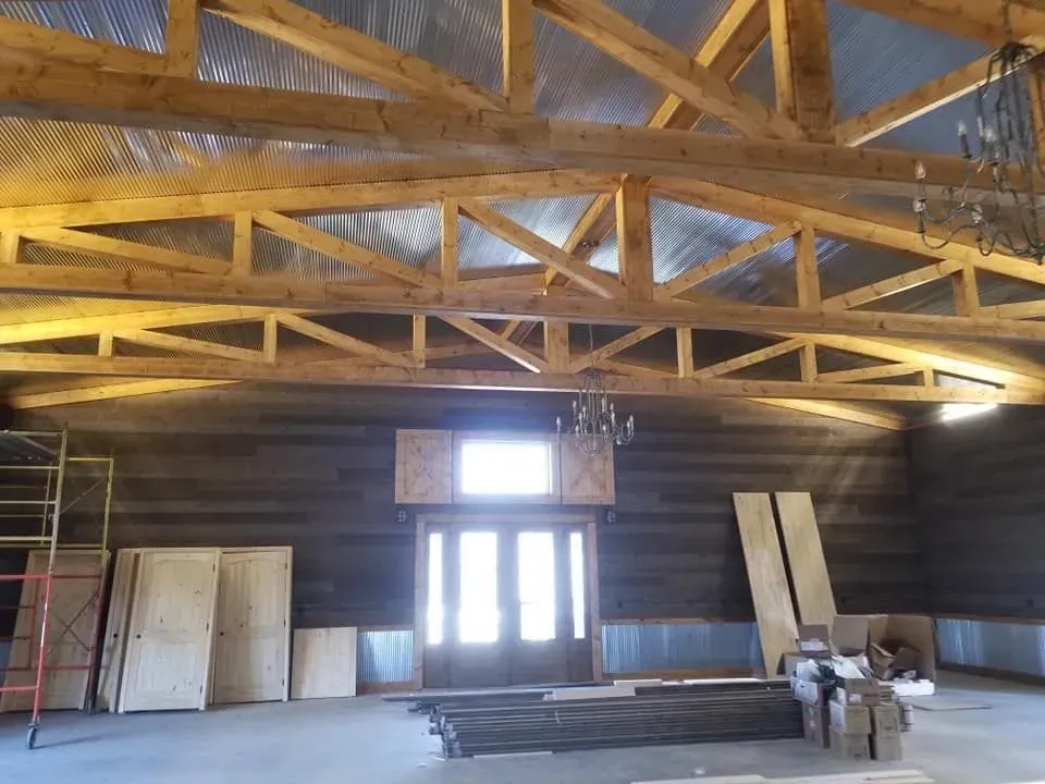 Interior view of a rustic building under construction, wooden beams, corrugated metal roofing, front door, and scaffolding.