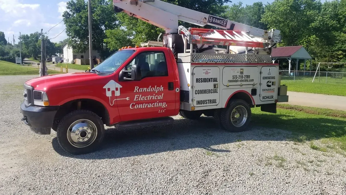 Red utility truck with aerial lift parked on gravel, used by New Look Electrical Construction.