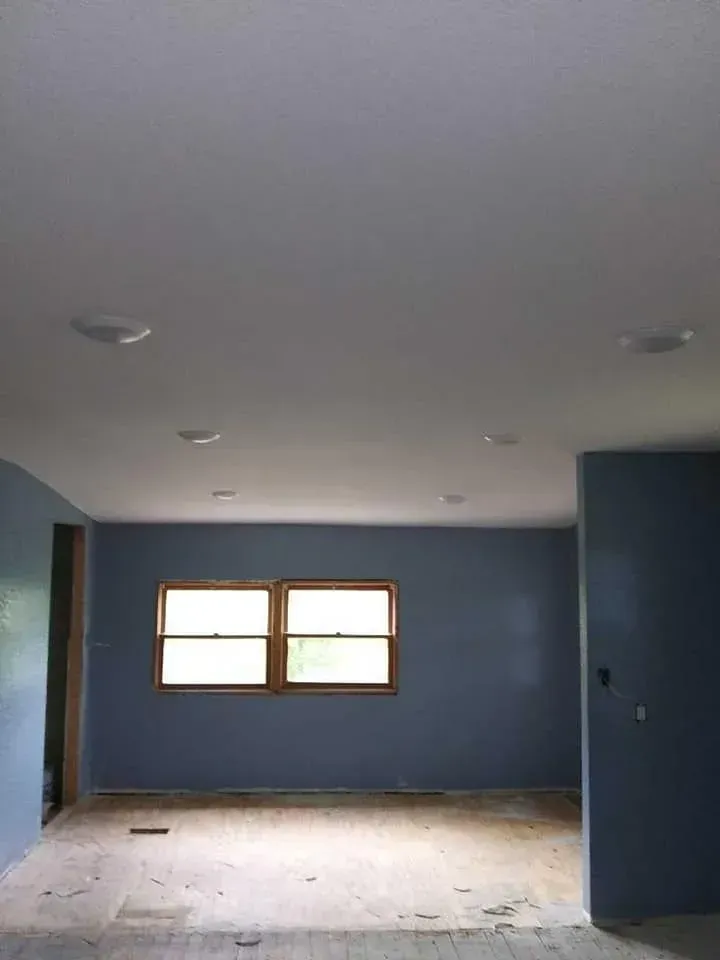 Empty room with blue walls, two windows, and recessed ceiling lights.
