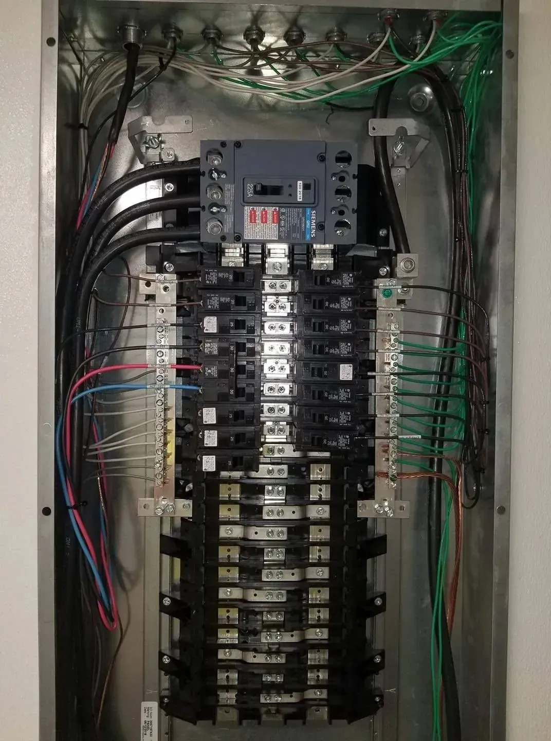 Electrical panel with circuit breakers and wiring, metallic box, indoors.