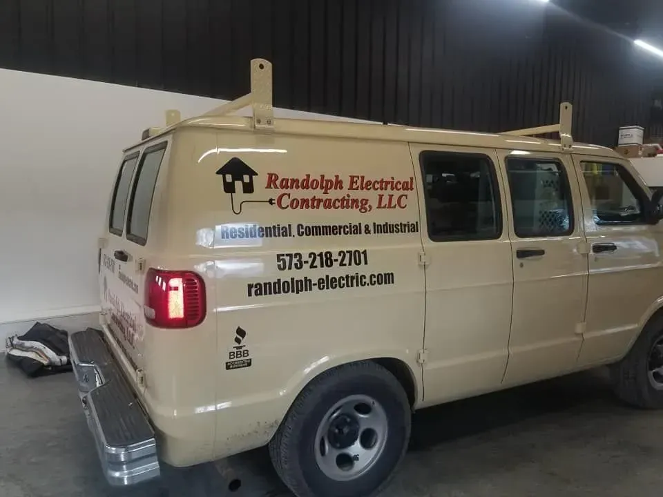 Beige work van for Randolph Electrical Contracting, LLC, with ladder rack, parked indoors.