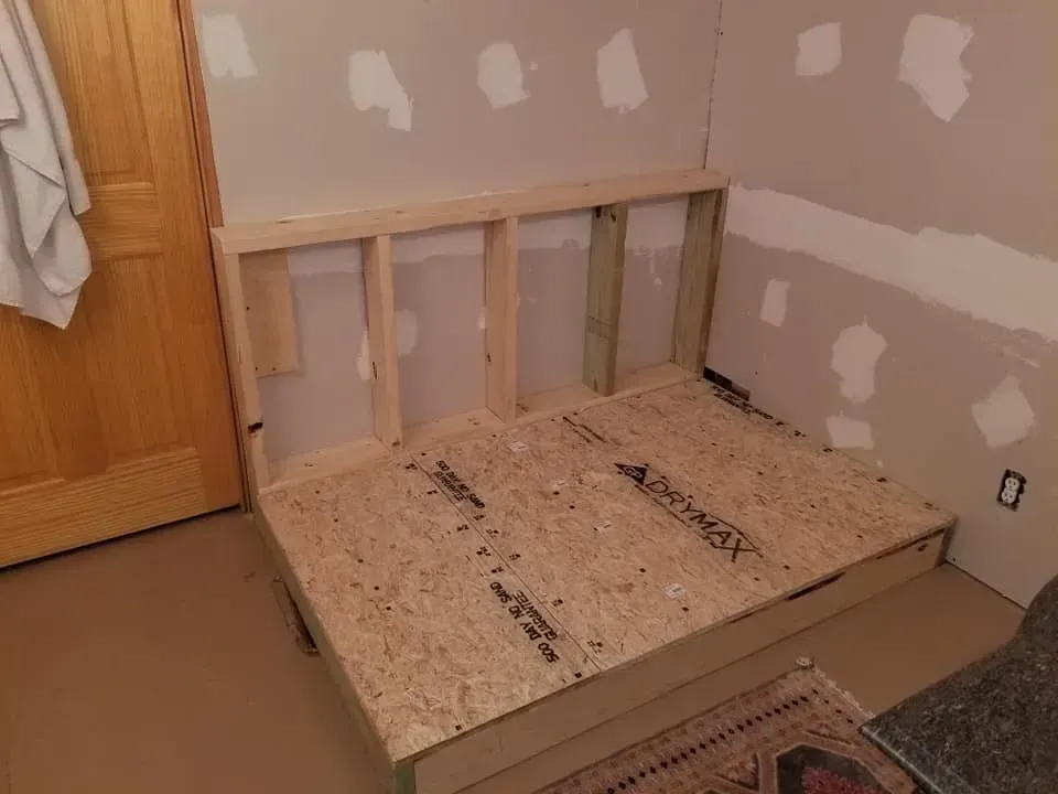 Wooden frame and platform being built in a room with unfinished walls.
