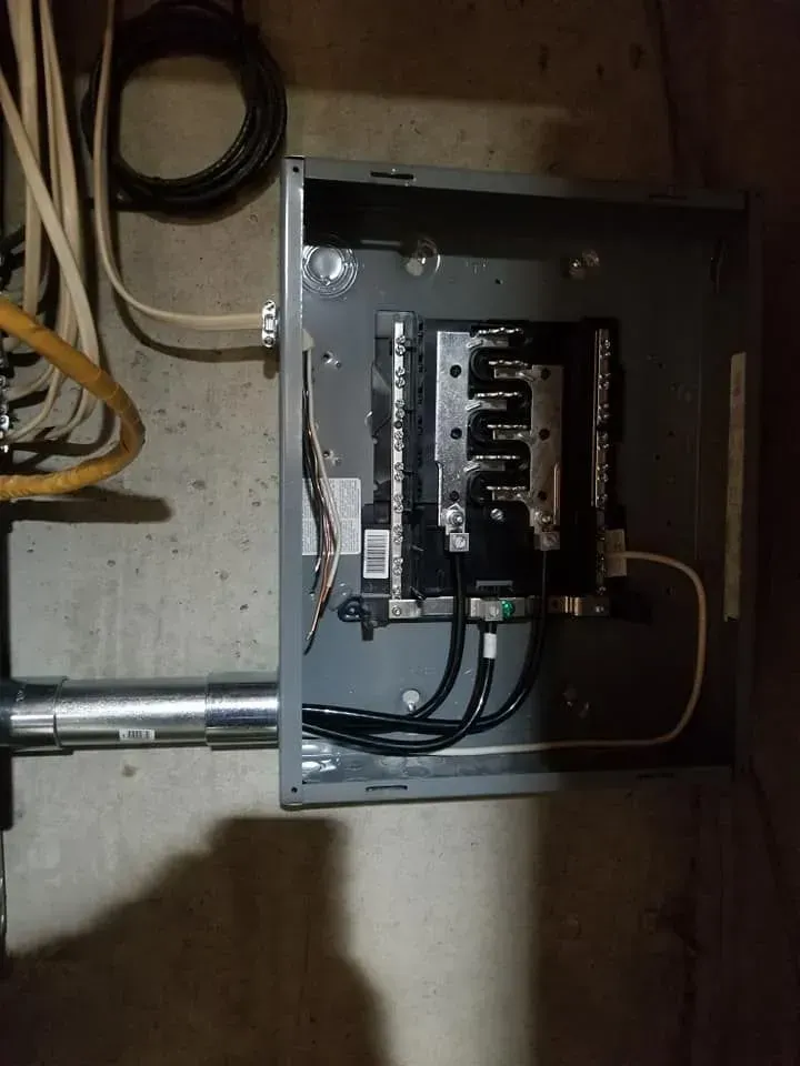 Gray electrical panel mounted on a concrete wall with conduit and wiring.