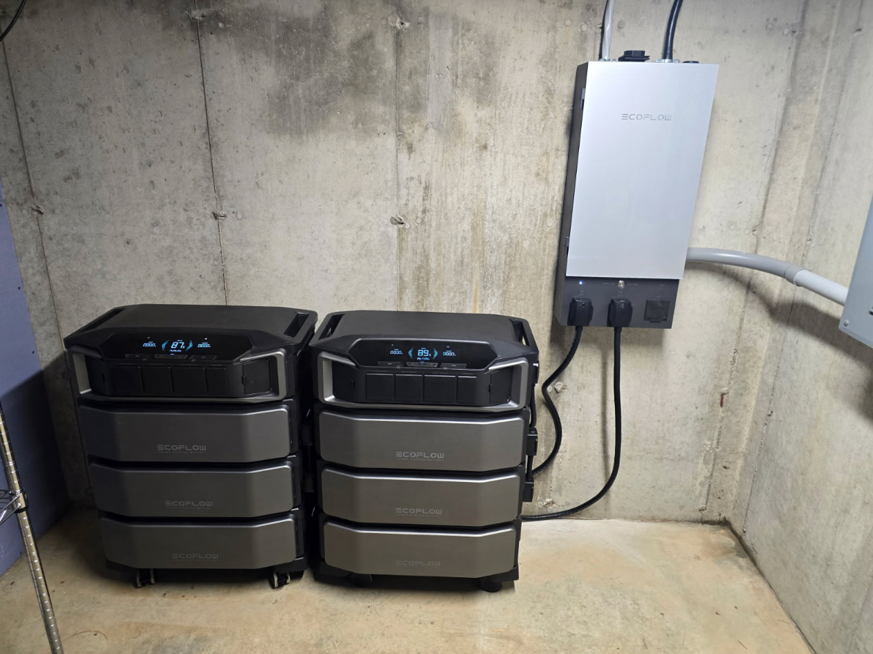 Two gray battery backup units next to a silver power inverter mounted on a concrete wall.