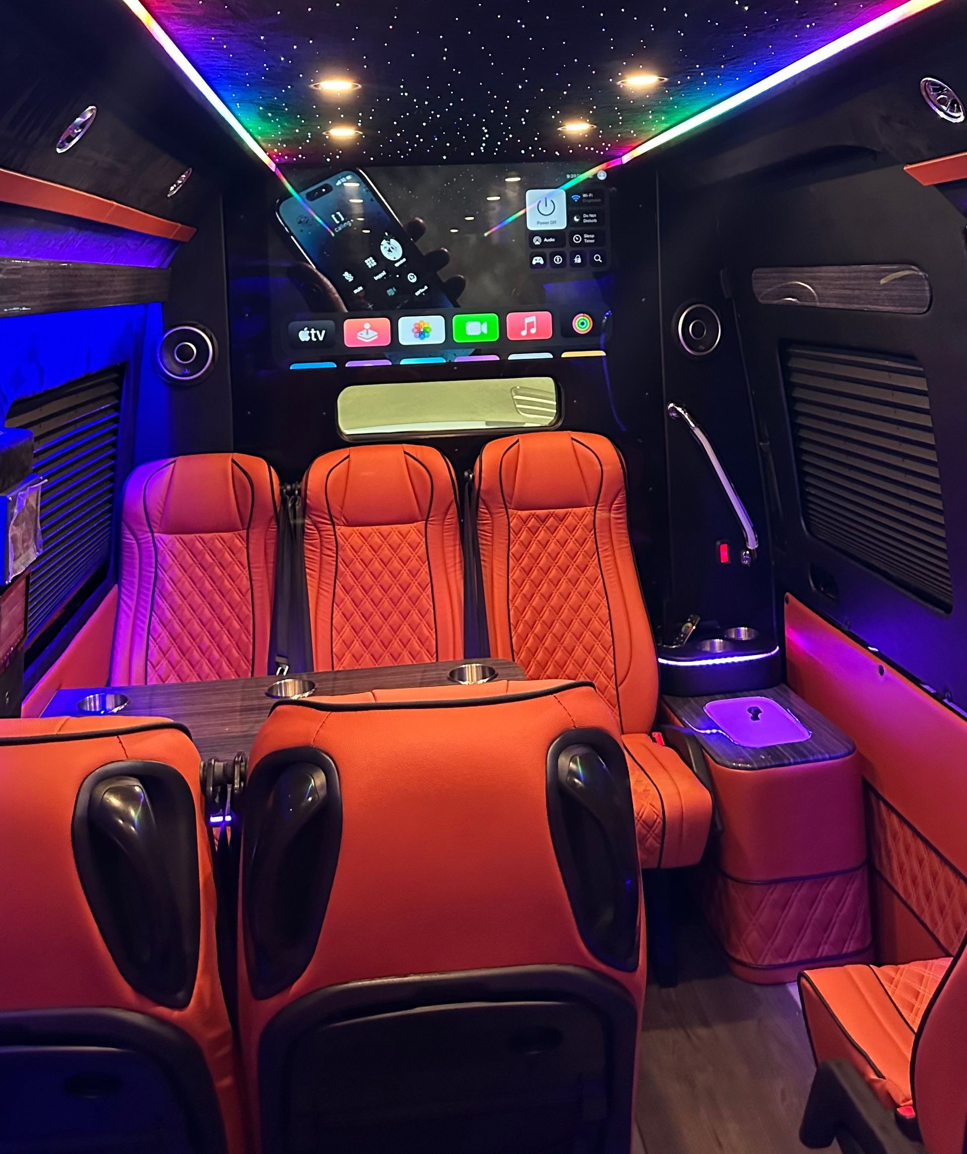 The inside of a van with red seats and a large screen on the ceiling.